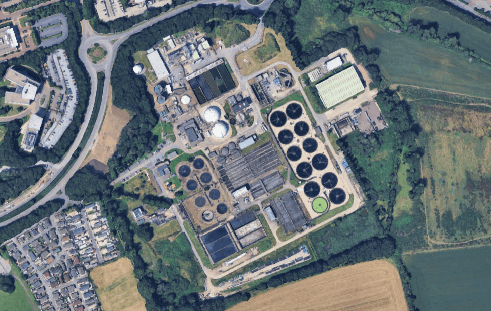 Aerial view of sewage treatment works seen from directly above and at some height, with neatly arrayed collection of circles denoting clarifier tanks, and other square and round structures also visible, set into green, semi-rural landscape