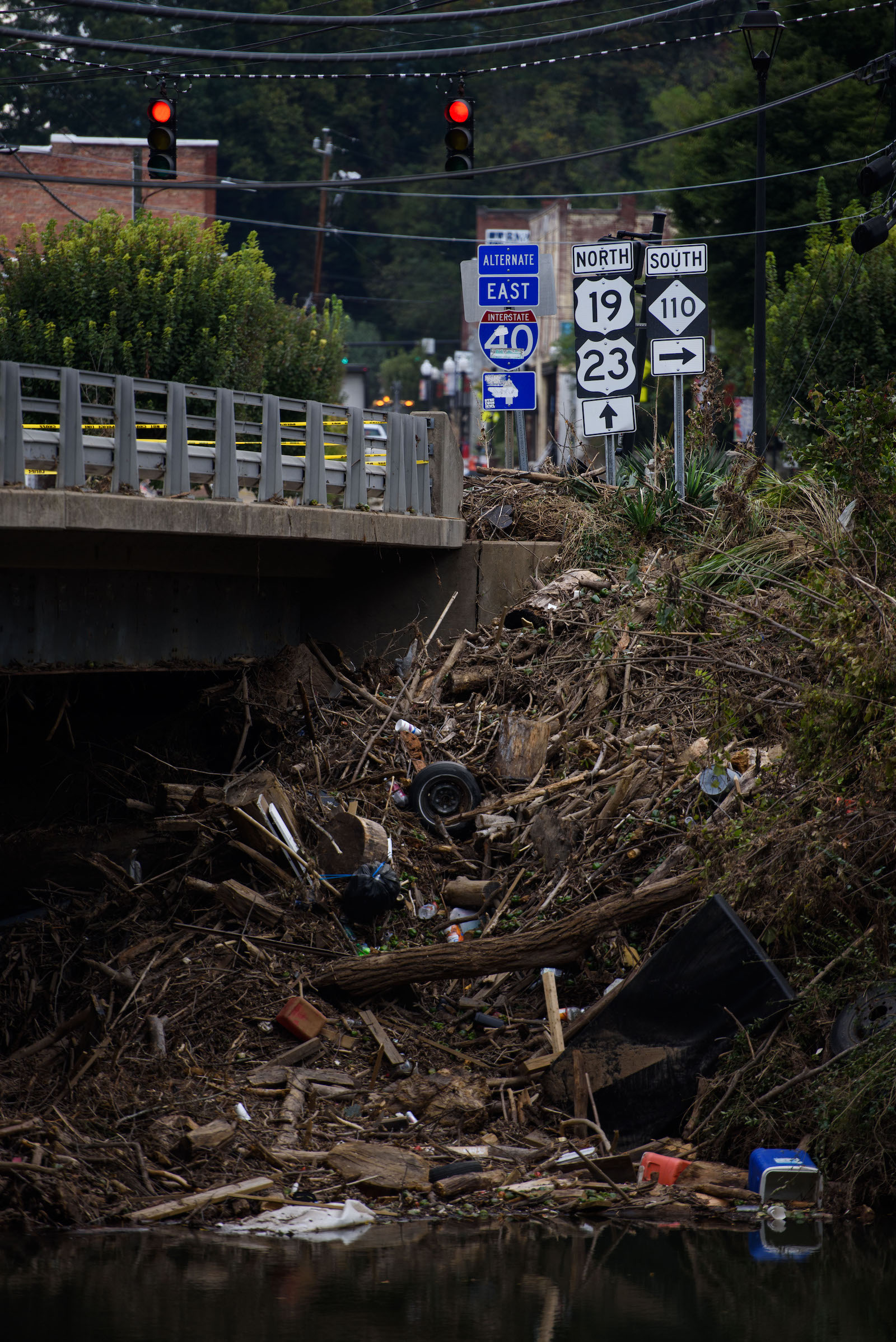 A giant pile of wood and trash runs from the top of a bridge all the way into a shallow river