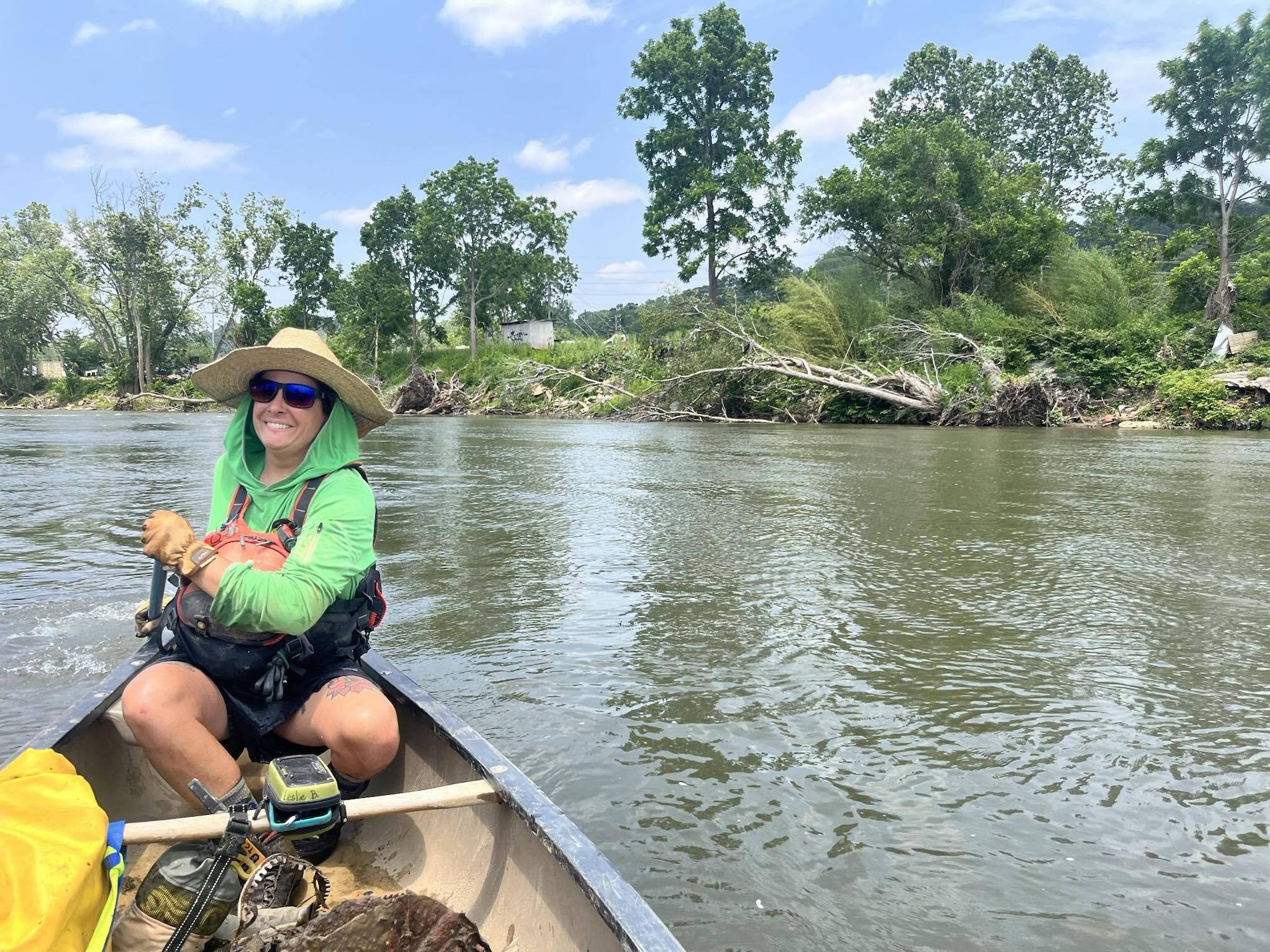 A river guide in a green jacket smiles while sitting in a kayak