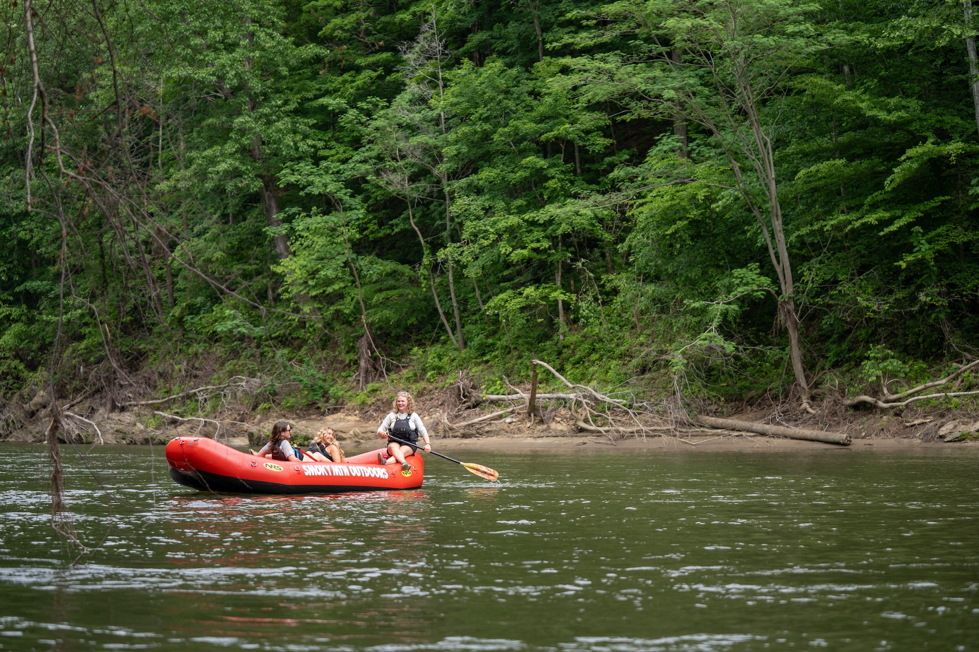 A young woman guides a river raft with two passengers in